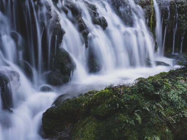 Beautiful waterfall cascading over lush green moss-covered rocks in a serene forest setting. Nature 4K
