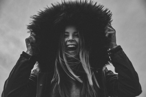 Black and white portrait of a joyful woman in a fur hood, radiating happiness. Charme 4K