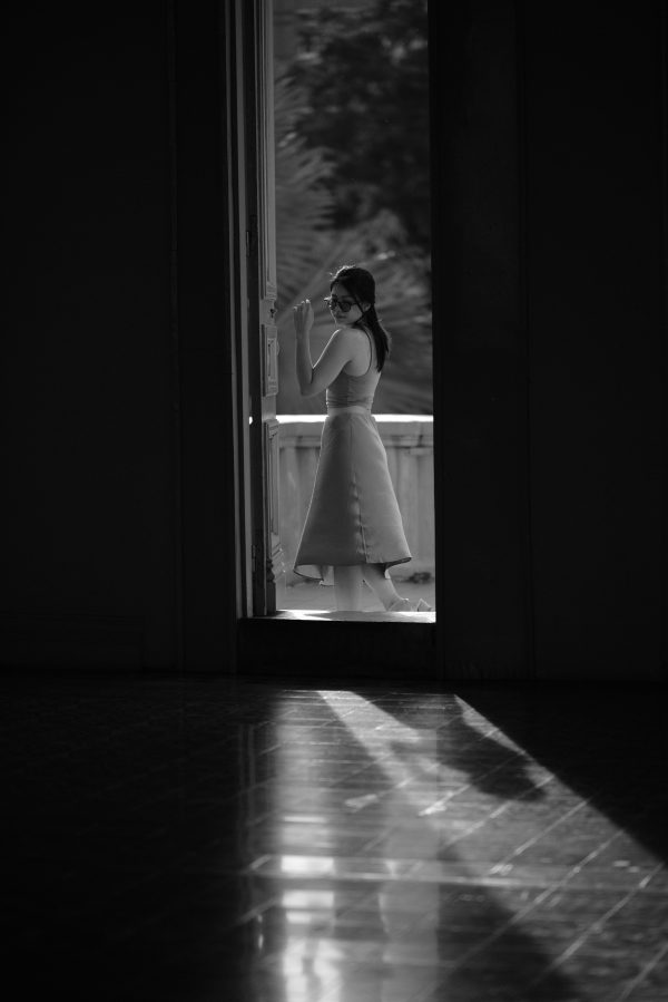 Black and white portrait of a woman in stylish attire standing by a window in Ho Chi Minh City, Vietnam. Mobile 4K