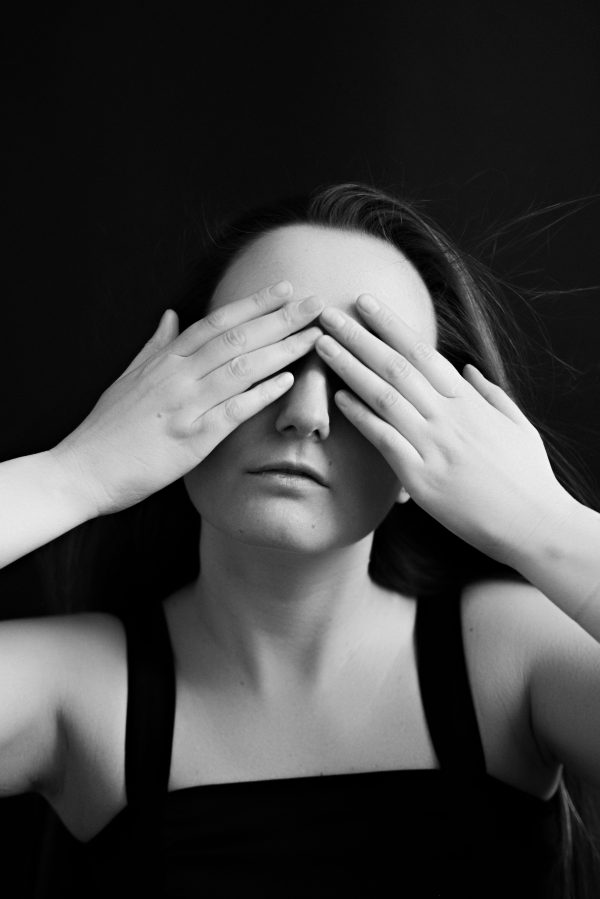 Black and white studio portrait of a woman covering her eyes with hands. Mobile 4K