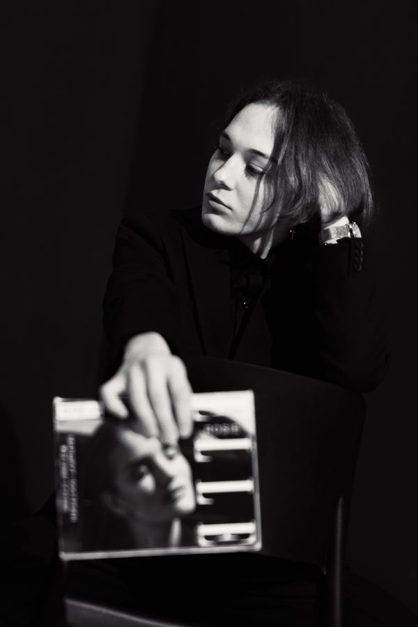 Black and white studio portrait of a young woman holding a magazine, exuding modern style. Mobile 4K