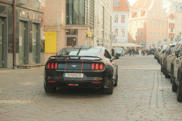 Black classic muscle car with racing stripes on a cobblestone city street. Voitures 4K