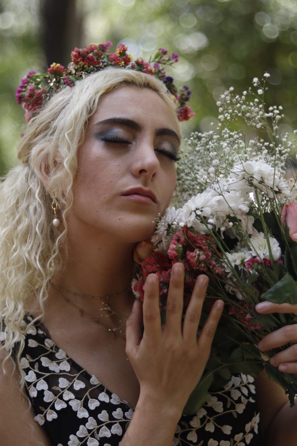 Blonde woman with floral crown holding bouquet, eyes closed, deep in thought. Mobile 4K