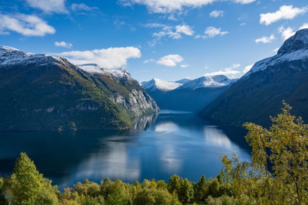 Breathtaking autumn view of a Norwegian fjord surrounded by snow-capped mountains and clear blue skies.