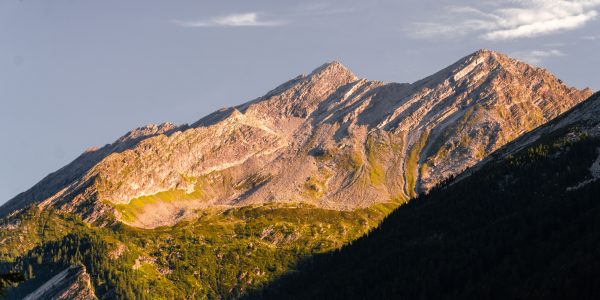 Breathtaking view of a sunlit mountain peak with lush greenery at sunset. Nature 4K