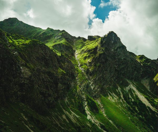 Breathtaking view of lush green mountain peaks under a dramatic cloudy sky, perfect for nature enthusiasts. Nature 4K