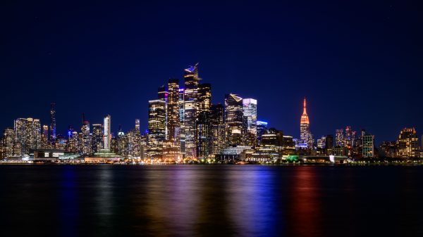 Breathtaking view of New York City skyline with vibrant city lights reflecting on water at night. Architecture 4K