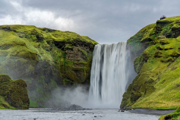 Breathtaking view of Skógafoss waterfall with lush green cliffs in Iceland, showcasing natural beauty. Nature 4K