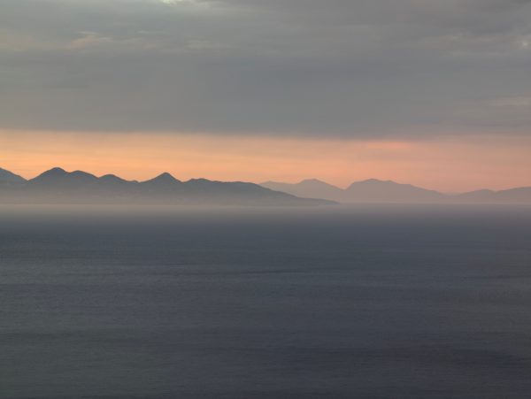 Calm sea at sunset with distant mountains under a soft, muted sky. Nature 4K