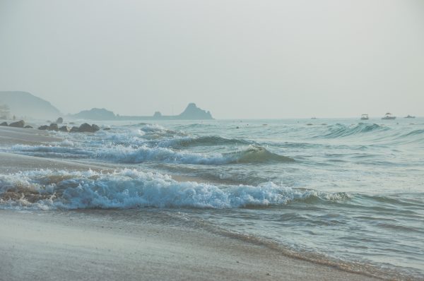 Calming scene of ocean waves on a misty beach with distant cliffs. Nature 4K