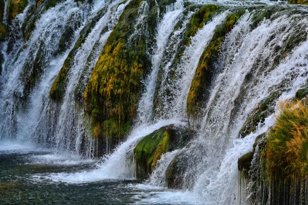 Captivating image of a waterfall flowing over lush, moss-covered rocks in a tranquil outdoor setting. Nature 4K