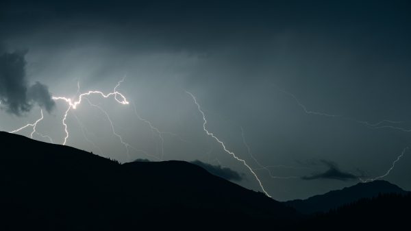 Captivating shot of lightning illuminating a dark sky over mountain silhouettes during a thunderstorm. Dark 4K