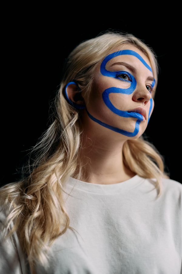 Captivating studio portrait featuring creative blue face paint on a blonde woman, set against a black background. Mobile 4K