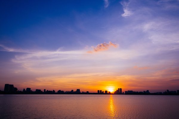 Captivating sunset with vibrant colors reflecting over calm water, silhouetted cityscape along the horizon. Nature 4K