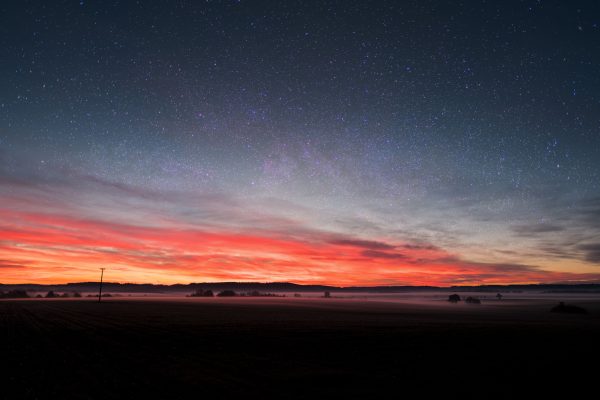 Captivating view of a starry sky blending with a vibrant sunset over a tranquil field. Nature 4K