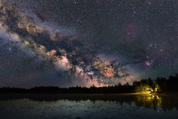Captivating view of the Milky Way galaxy reflecting over a serene lake surrounded by trees at night. Espace 4K