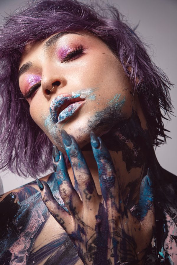 Chic portrait of a woman with purple hair, artistic face paint, and creative makeup. Studio shoot in Colombia. Mobile 4K