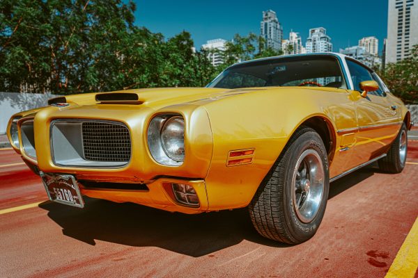Classic yellow Pontiac car parked outdoors, showcasing luxury and retro charm with Dubai skyline in the background. Voitures 4K