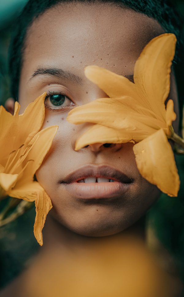 Close-up artistic portrait of a woman partially obscured by vibrant yellow flowers. Mobile 4K