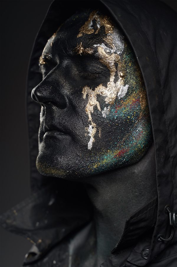 Close-up artistic portrait of an adult with black and gold face paint in a moody setting. Mobile 4K