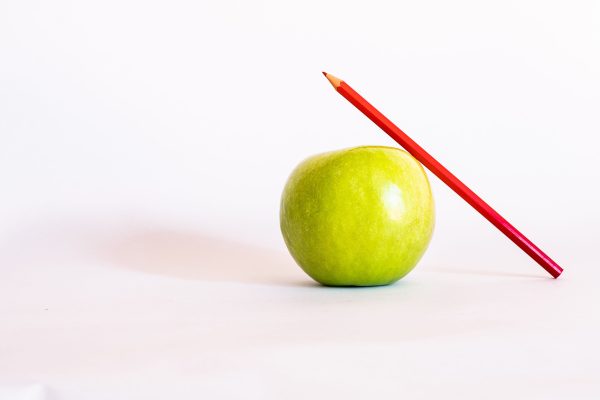 Close-up of a green apple with a red colored pencil against a white background. Minimaliste 4K