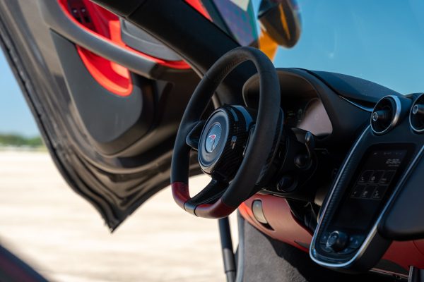 Close-up of a McLaren interior featuring a sleek steering wheel and open gullwing door, showcasing luxury design. Voitures 4K