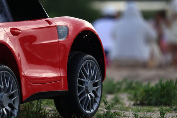 Close-up of a red toy car's front wheel and body on grass. Blurred background. Voitures 4K