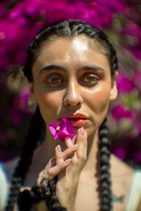 Close-up portrait of a woman holding a bugambilia flower, set against a vivid floral background. Mobile 4K
