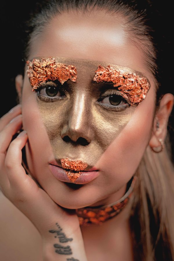 Close-up portrait of a woman with metallic face paint and copper accents. Mobile 4K