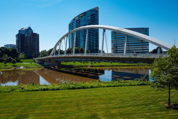 Contemporary bridge spanning a river with city buildings in the background on a sunny day. Architecture 4K
