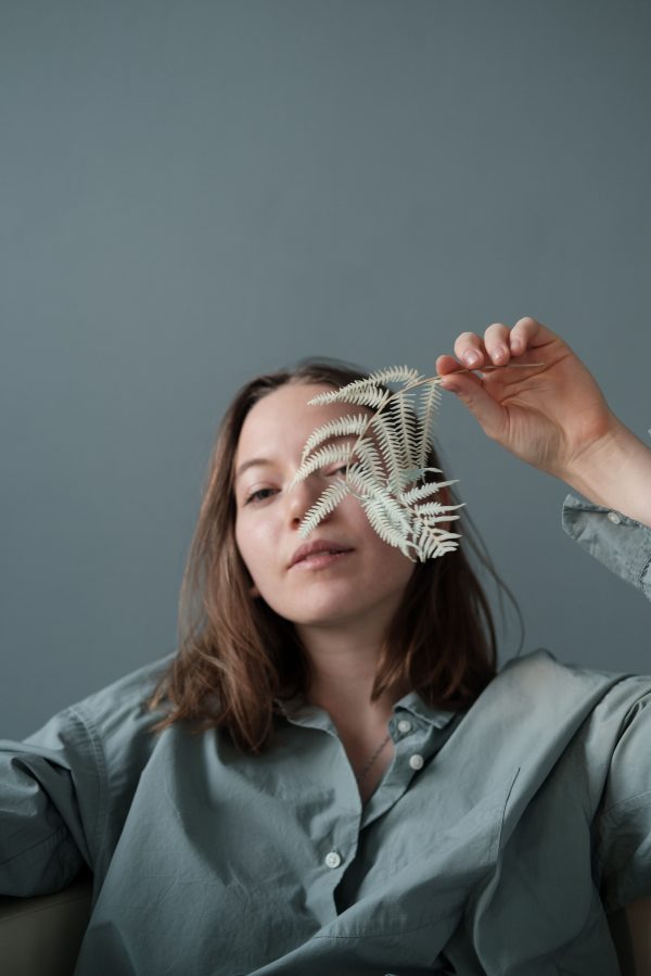 Delicate female in casual wear hiding face behind branch of plant with green leaves at home Mobile 4K