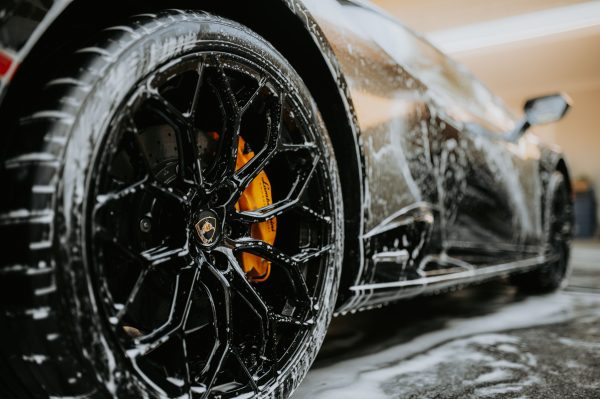 Detailed close-up of a luxury car wheel covered in soap suds during a professional car wash. Voitures 4K