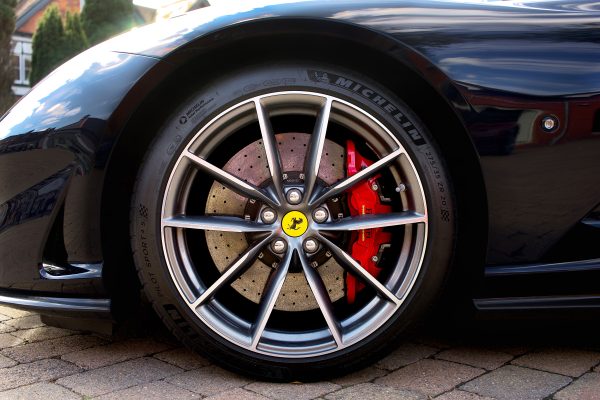 Detailed image of a Ferrari sports car wheel with red brake caliper, shot outdoors. Voitures 4K