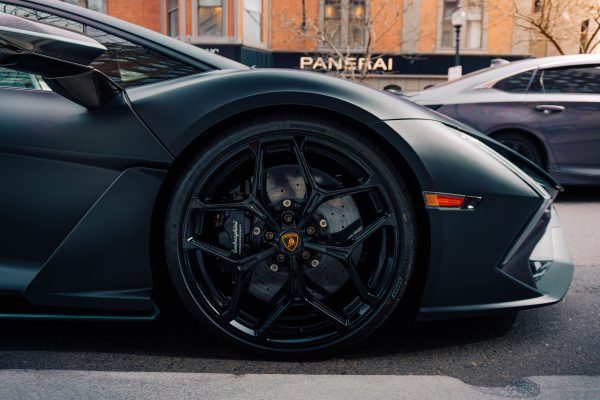 Detailed view of a luxury car wheel in an urban setting, showcasing sleek design. Voitures 4K