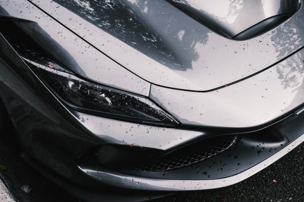 Detailed view of a luxury silver car with raindrops, highlighting sleek design and headlight features. Voitures 4K