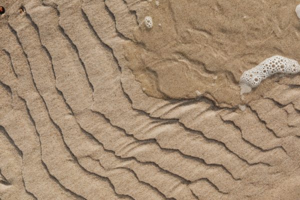 Detailed view of rippled sand patterns with sea foam on a sunny beach. Nature 4K