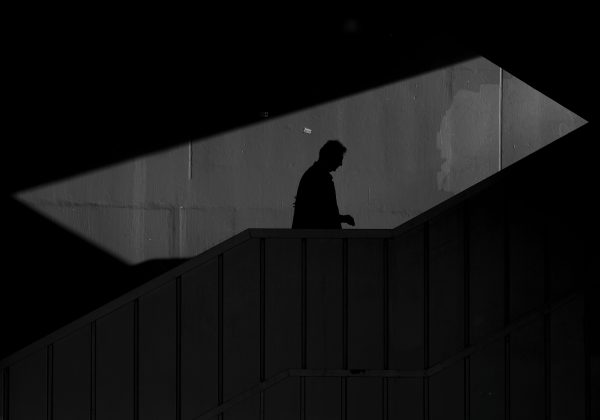 Dramatic black and white image of a person's silhouette walking down a staircase. Dark 4K