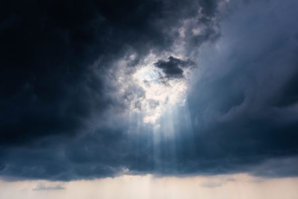 Dramatic sky with sun rays breaking through dark stormy clouds, creating a majestic view. Dark 4K
