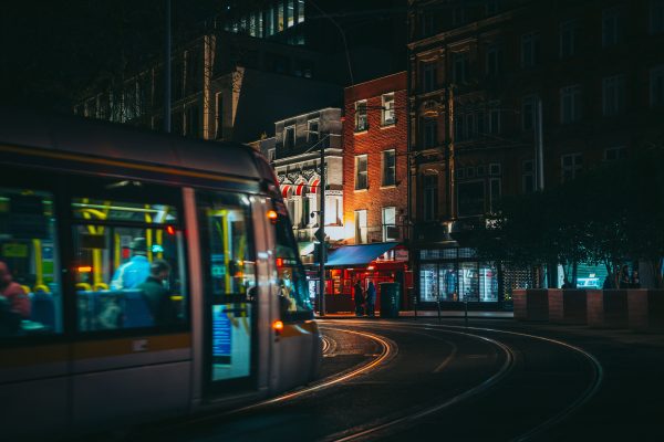 Dynamic city night scene with a moving tram passing illuminated shops. Voitures 4K