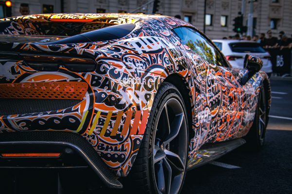 Dynamic image of a sports car with a vibrant graffiti-style wrap, captured on a bustling city street. Voitures 4K