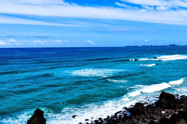 Dynamic seascape with vibrant waves hitting rocky shore under bright blue sky. Nature 4K