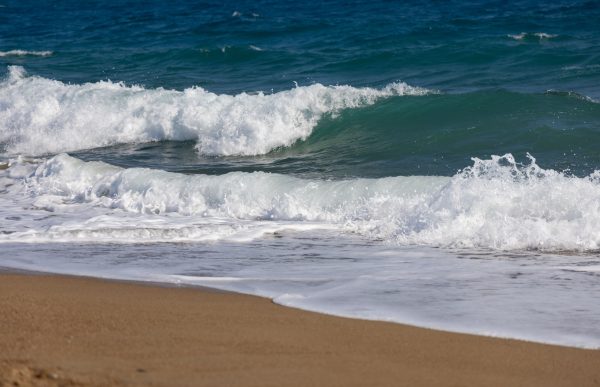 Dynamic waves crash on a sandy beach, showcasing vivid ocean colors and natural beauty. Nature 4K