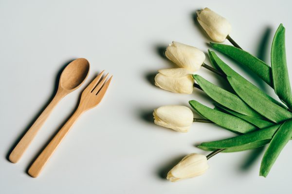 Elegant arrangement of wooden fork and spoon with cream tulips on a light background. Minimaliste 4K
