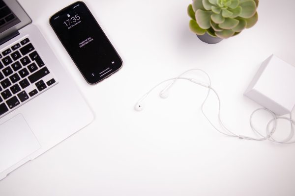 Elegant minimalist workspace featuring a laptop, smartphone, earbuds, and succulent on a white desk. Minimaliste 4K