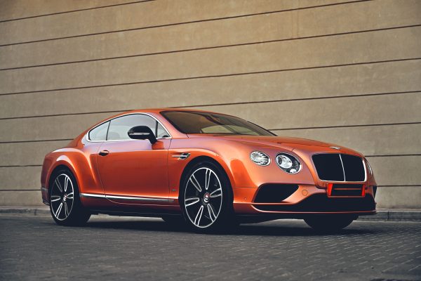 Elegant orange Bentley car parked in front of a modern architectural wall, showcasing luxury and style. Voitures 4K