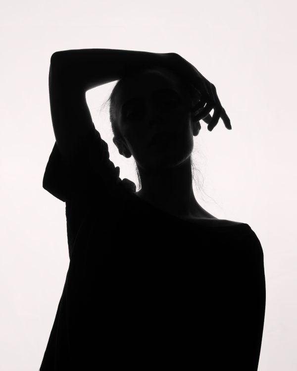 Elegant silhouette portrait of a person posing with hand on head against a bright background. Mobile 4K