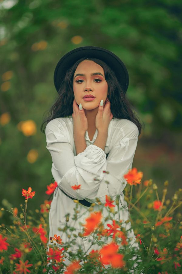 Elegant woman posing in white dress and black hat surrounded by red flowers in summer meadow. Mobile 4K