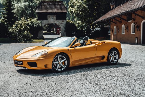 Elegant yellow Ferrari convertible parked in a sunlit, scenic courtyard showcasing luxury and style. Voitures 4K