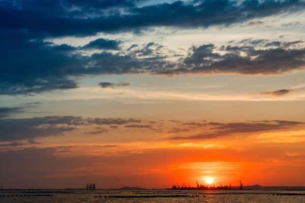Epic sunset view over the sea with silhouettes of industrial cranes on the horizon. Nature 4K