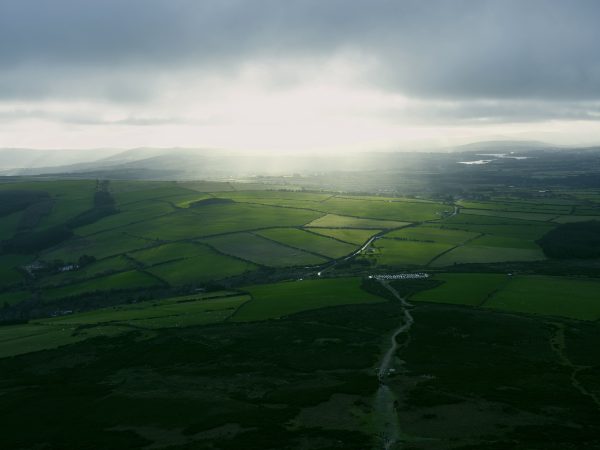 Expansive green fields under dramatic sky with sunrays breaking through clouds, captured from above. Nature 4K